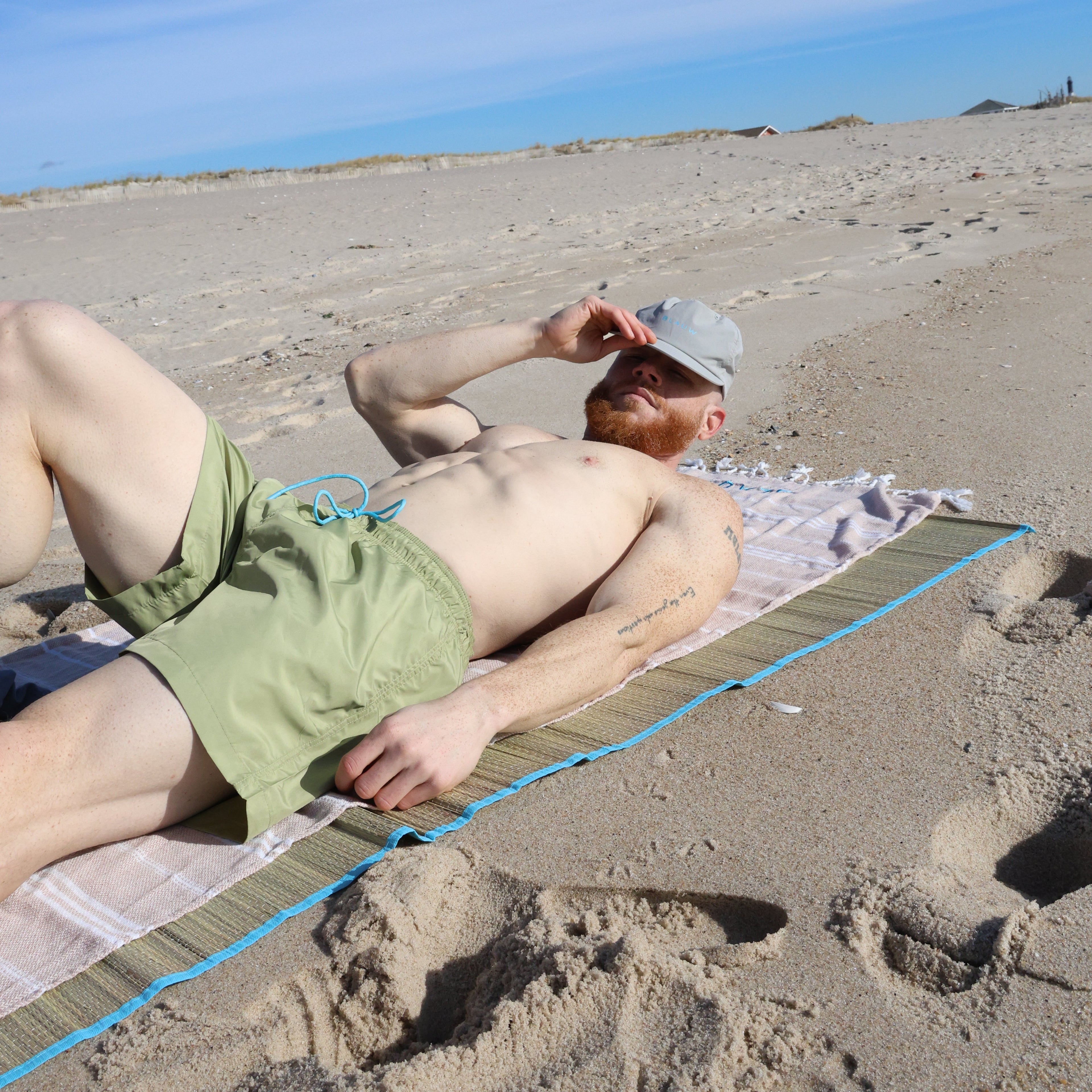 Person lying on a towel at the beach showcasing green swim short from ocean plastic