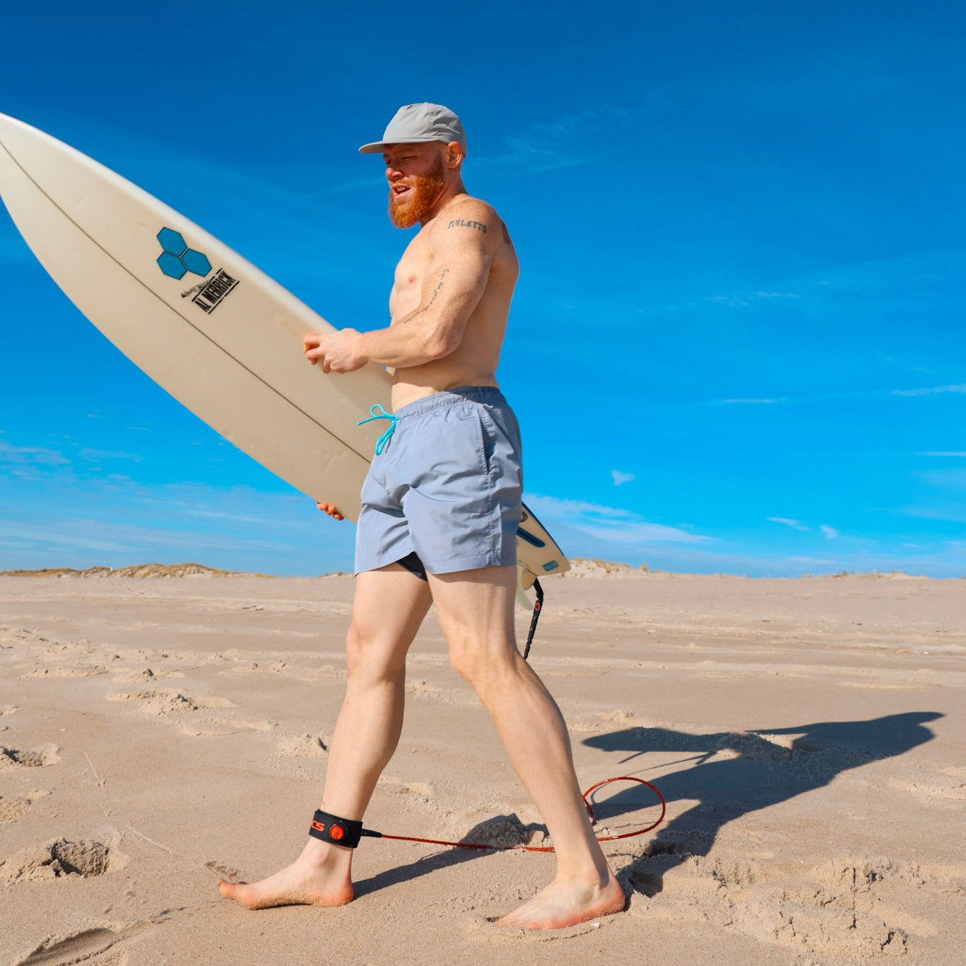Man walking on a sandy beach holding a surfboard while wearing sustainable swimwear