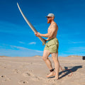Man holding a surfboard on a sandy beach wearing a comfortable swim short from ocean plastic.