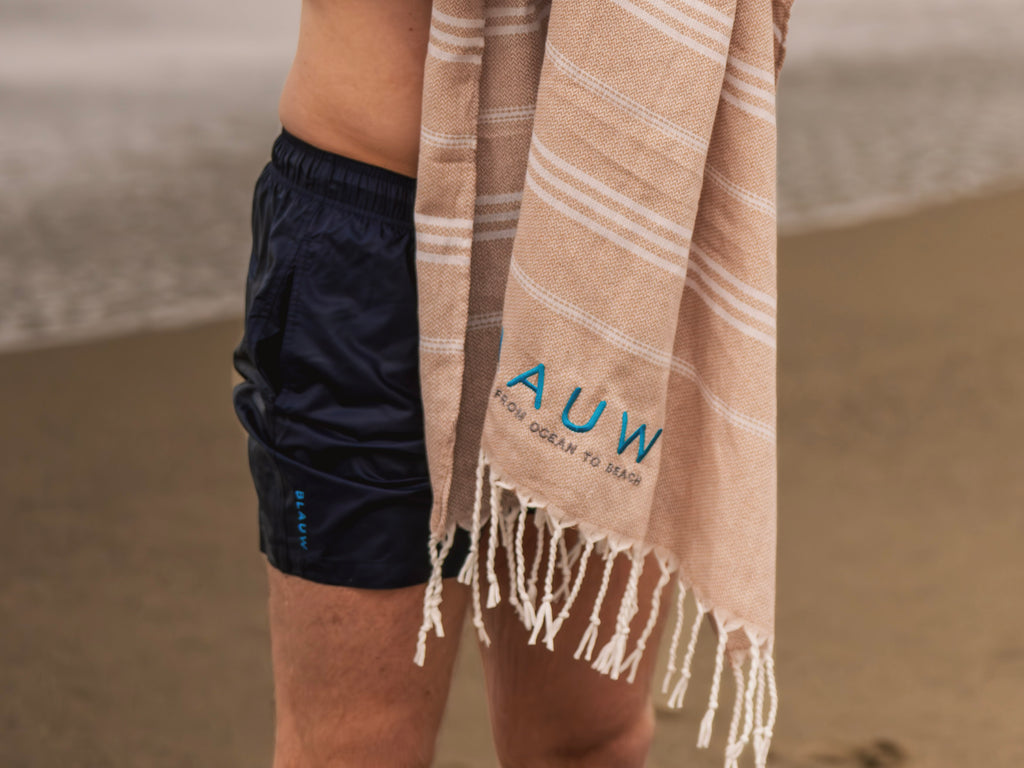 Man wearing recycled swim shorts drying off with a sustainable beach towel; sustainable swimwear and towel made for ocean lovers.