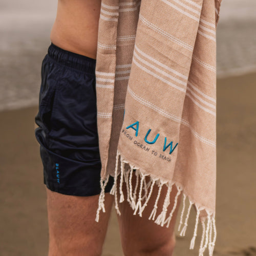 Man wearing quick dry swim shorts drying off with a sustainable beach towel