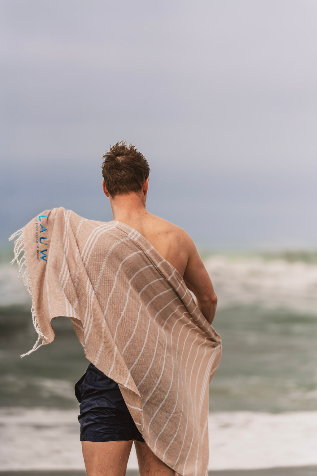 Man wearing sustainable swim shorts drying off with a recycled beach towel; sustainable swimwear and towel made for ocean lovers.