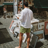 A man viewed from behind wearing a white long-sleeve linen shirt and olive green shorts that can be worn all-day