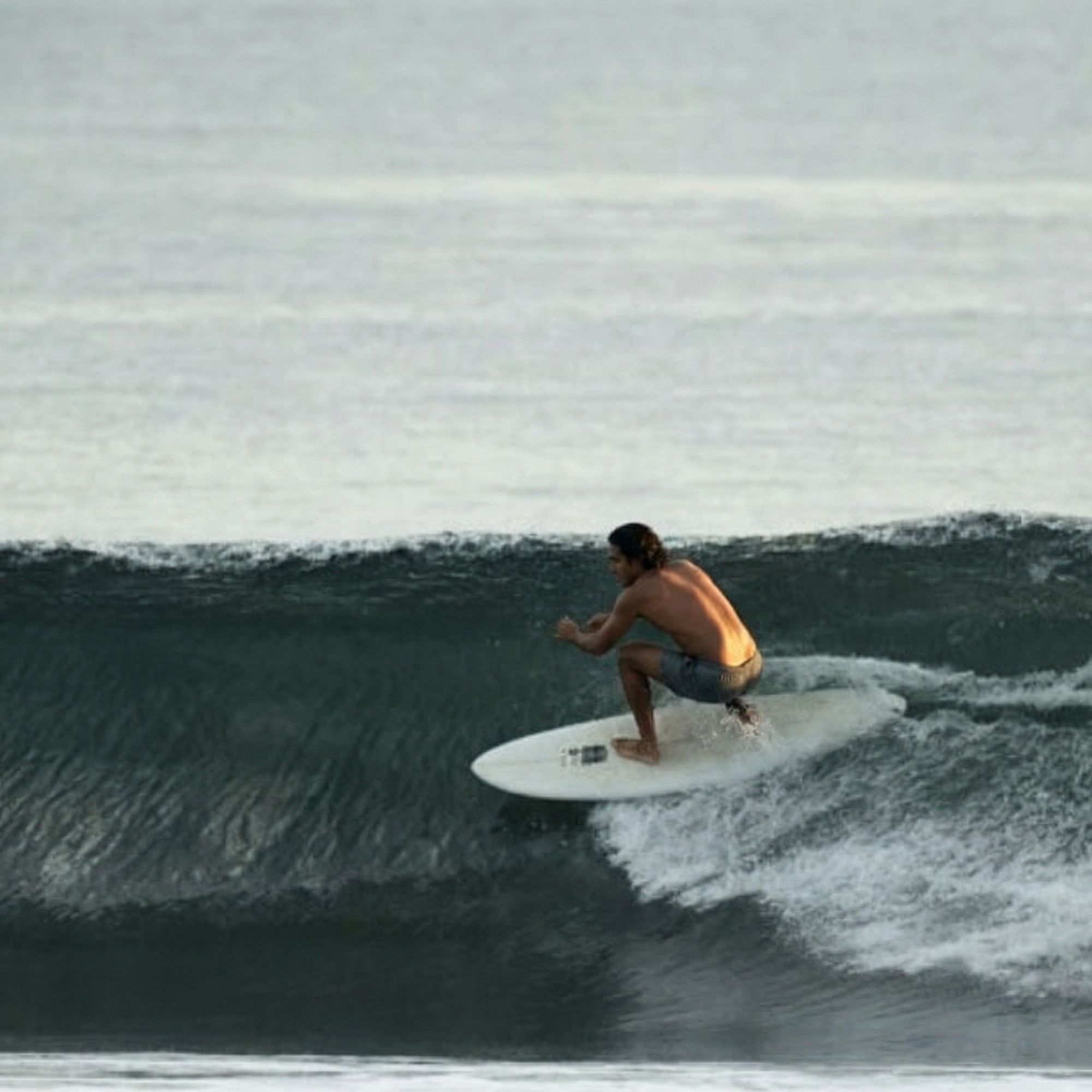 Person surfing on a wave in the ocean wearing recycled swim trunks