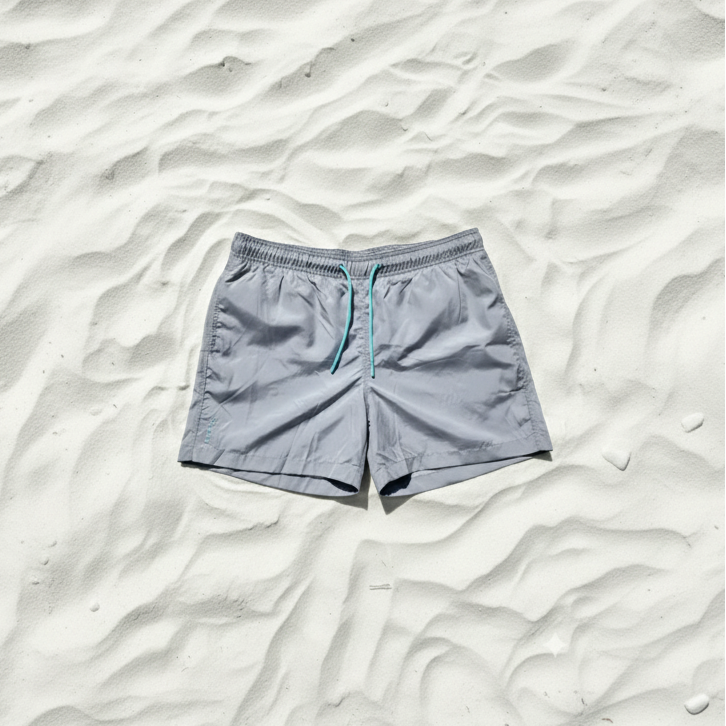 Gray swim shorts from ocean plactic with a blue drawstring on a sandy background