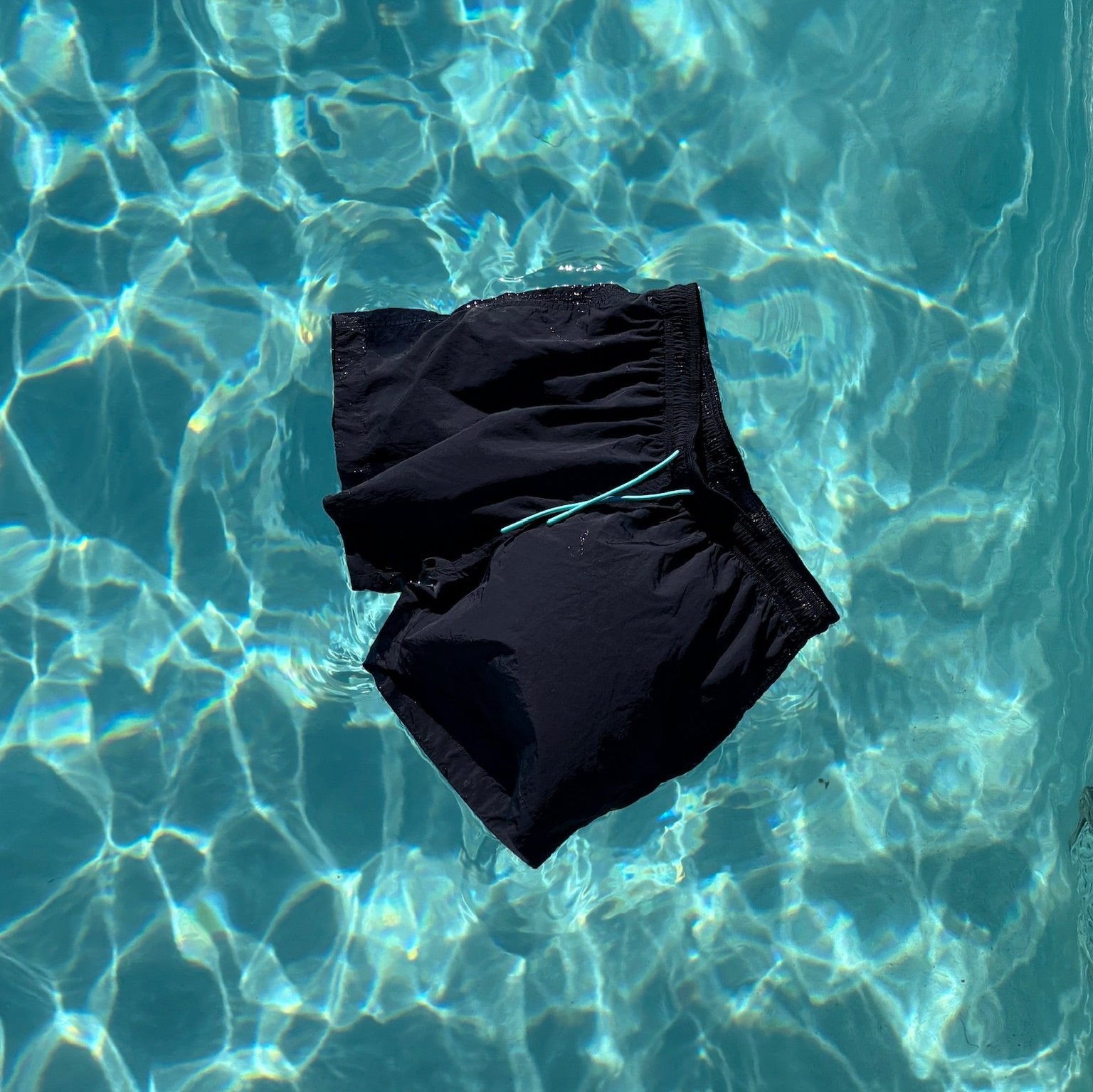 Navy blue recycled swim shorts floating in clear ocean water, made from 100% recycled plastic