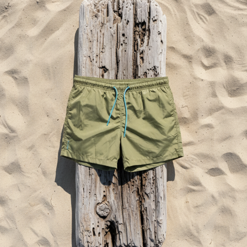 Green recycled swim shorts on a wooden block against a sandy background